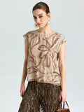 A woman stands against a plain light background wearing the Social Queen Floral Sequin Embroidered Silk Top, paired with a brown fringe skirt, statement earrings, and holding a brown bag.
