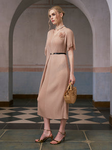 A woman stands in an arched hallway wearing the Social Queen Asymmetric Fringe Midi Dress (belt included), paired with gold heels and a wooden handbag.
