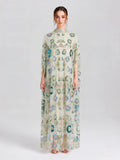 A woman faces forward in the Social Queen Beaded Floral Embellished Cape Gown, a floor-length dress with colorful floral detailing and a high neck, set against a simple light background.