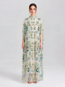 A woman faces forward in the Social Queen Beaded Floral Embellished Cape Gown, a floor-length dress with colorful floral detailing and a high neck, set against a simple light background.