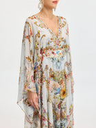 A woman models the Baroque Floral Print Silk Caftan Dress by Social Queen, featuring a flowing caftan silhouette, V-neck, wide sleeves, and colorful floral and baroque-inspired patterns against a plain backdrop.