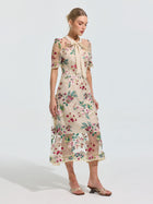 A woman models the Social Queen Floral Embroidered Bow-Tie Dress, a sheer mesh A-line design with floral embroidery, bow-tie neck, and short sleeves, set against a plain background.