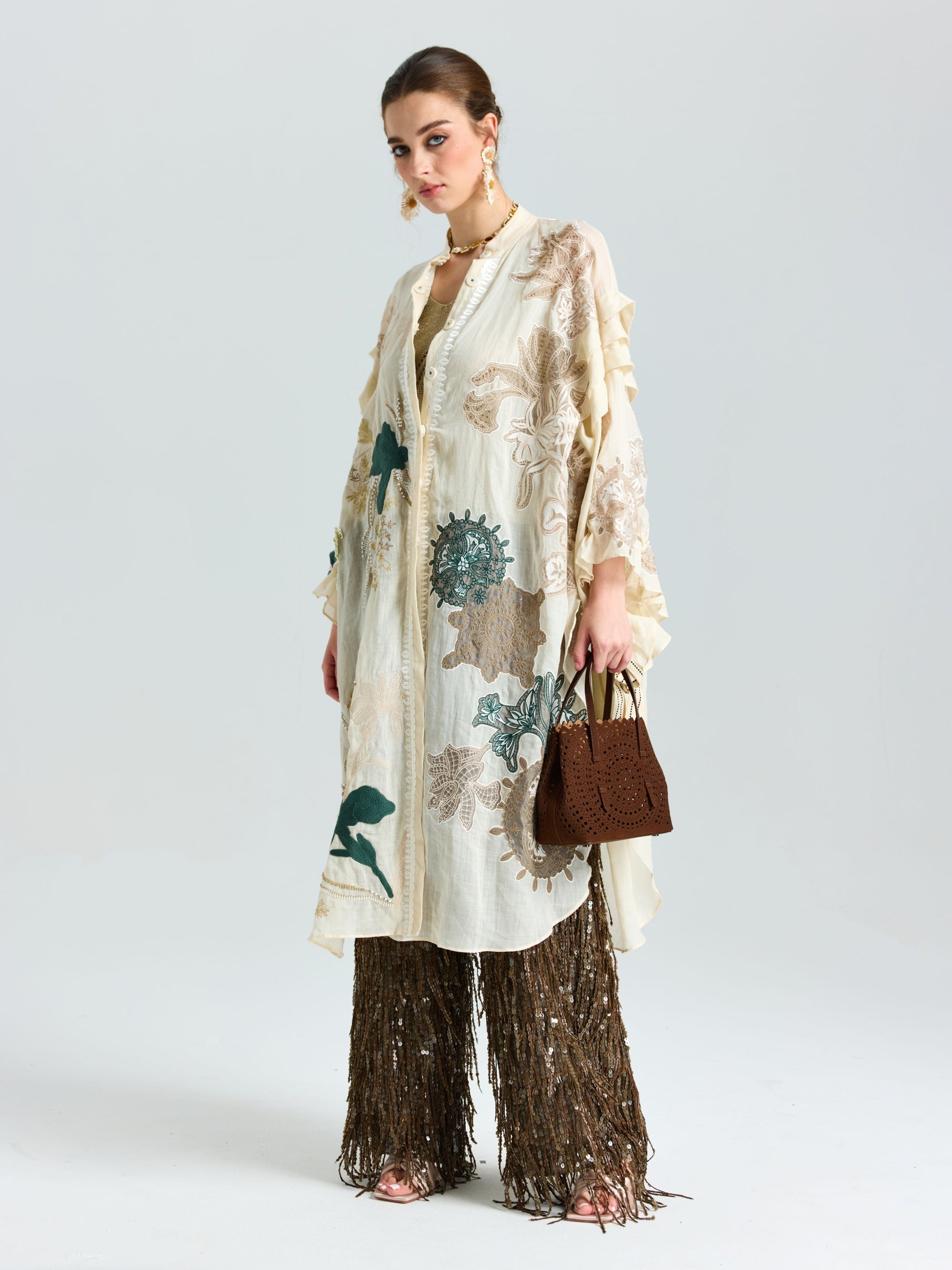 A woman models Social Queen’s Floral Embroidered Linen Jacket (Cami Included), styled over brown sequined fringe pants with a matching brown handbag, standing against a plain white background.