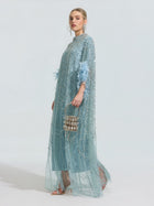 A person wears the Social Queen Beaded Embroidered Feather Trim Cape Gown and holds a small embellished handbag while standing against a plain light background.