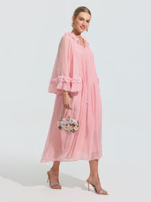 A woman models the Social Queen 3D Floral Embellished Silk Dress—a loose, light pink midi with ruffled sleeves—paired with a small floral handbag and heeled sandals against a plain light background.