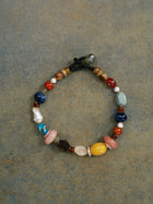 Displayed on a textured surface, the Social Queen Multicolor Stone Beaded Necklace showcases an array of vibrant stones and beads strung on a black cord, capturing the lively charm of handcrafted jewelry.