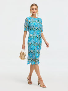 A woman wears the Social Queen Floral Appliqué Lace Shift Dress with gold earrings, gold heeled sandals, and carries a small beige handbag while walking against a plain white background.