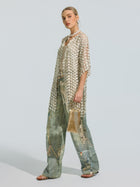 Wearing the Social Queen Pearl Daisy Cutwork Long Cardigan, adorned with delicate pearl embellishments over a tank and wide-leg jeans, and accessorized with a small gold purse, the person stands against a plain background.