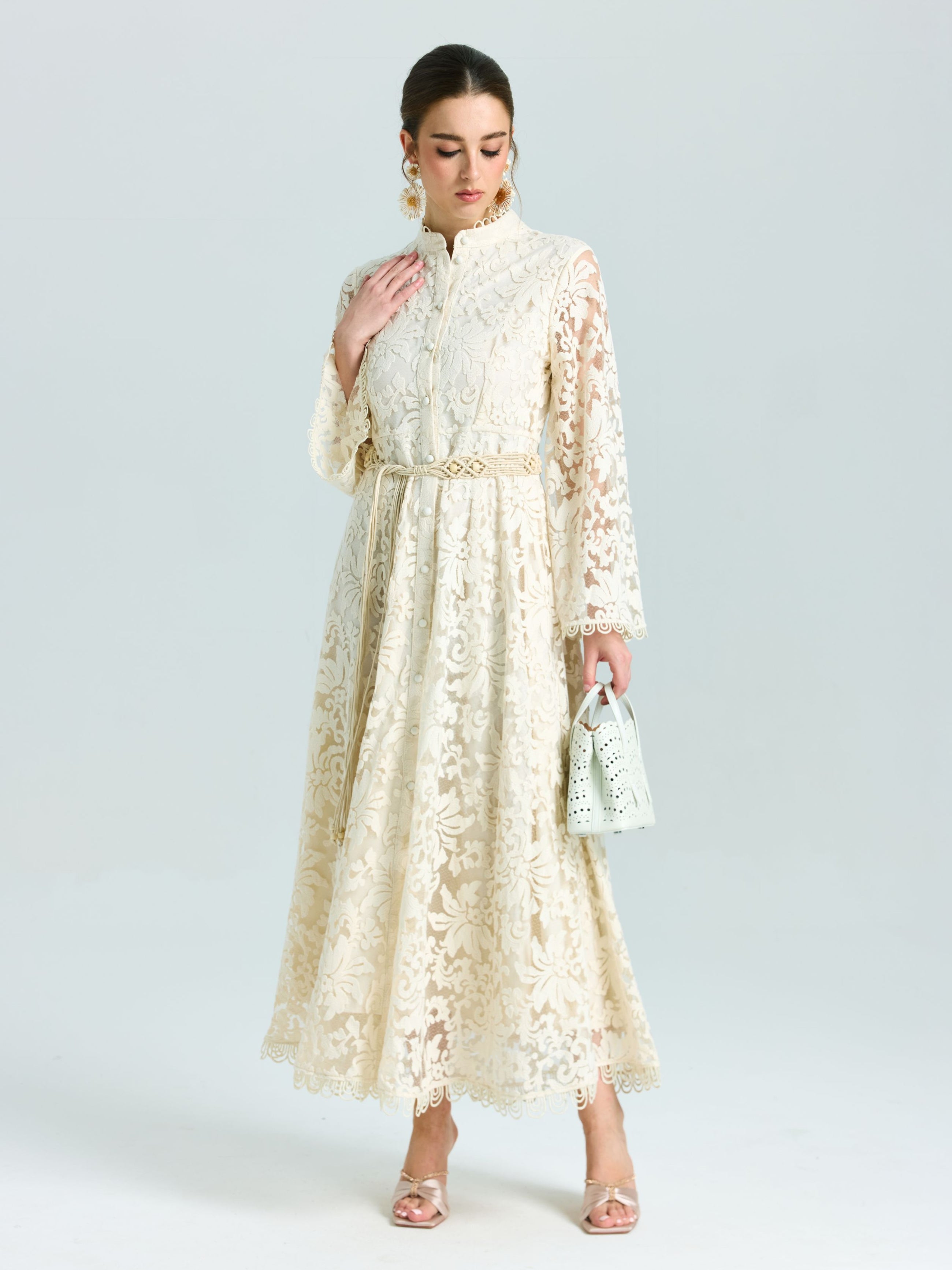 A woman wears the Social Queen Embroidered Lace High-Neck Dress with a small handbag, heeled sandals, and statement earrings. Her hair is tied back.