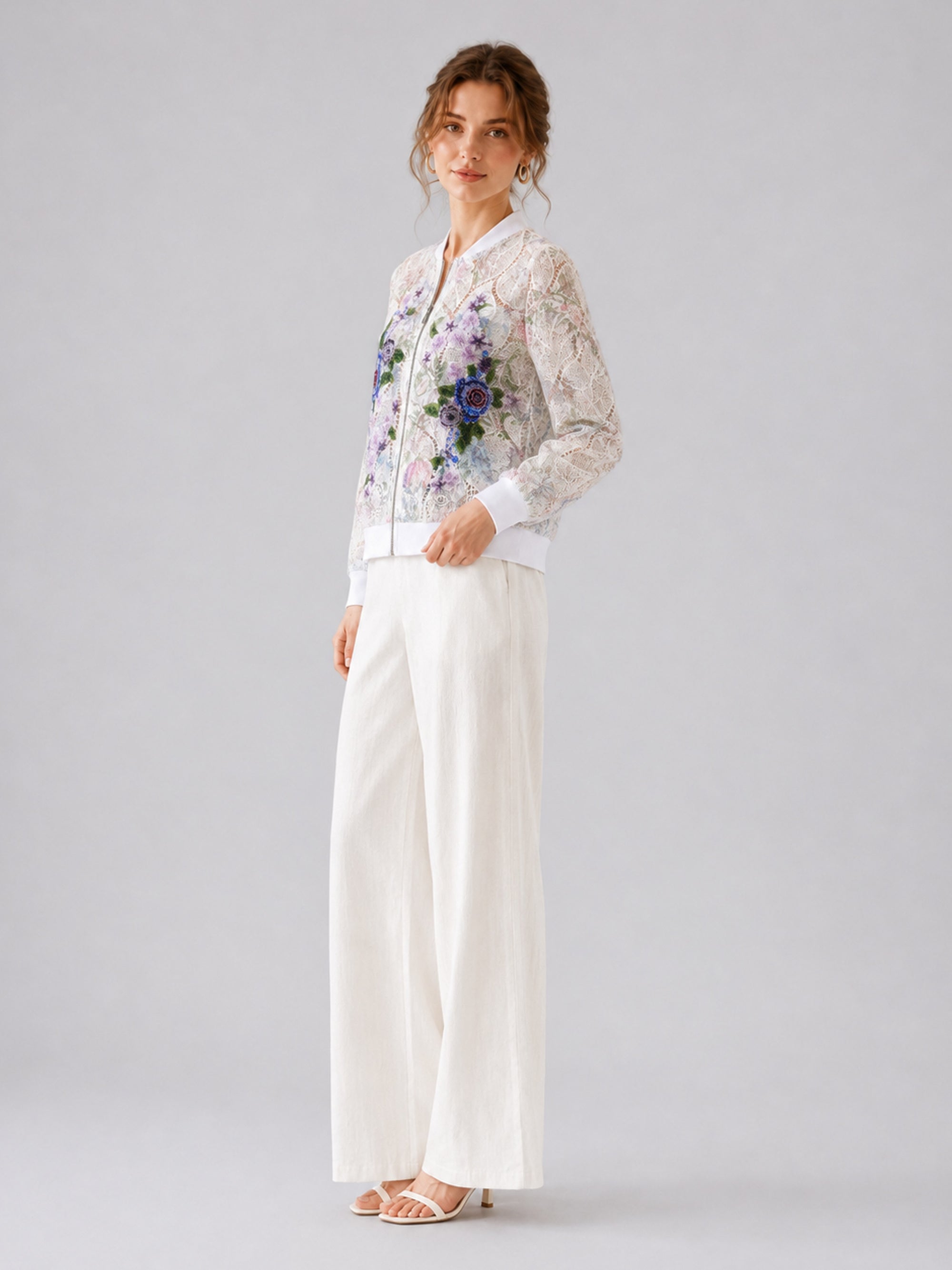 A woman stands against a plain light gray background wearing Social Queen’s Casual Wide-Leg Pants, paired with white heeled sandals and a sheer floral-embroidered jacket.