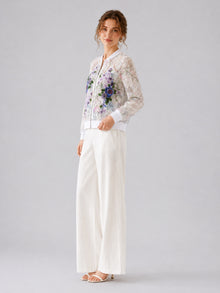 A woman stands against a plain light gray background wearing Social Queen’s Casual Wide-Leg Pants, paired with white heeled sandals and a sheer floral-embroidered jacket.
