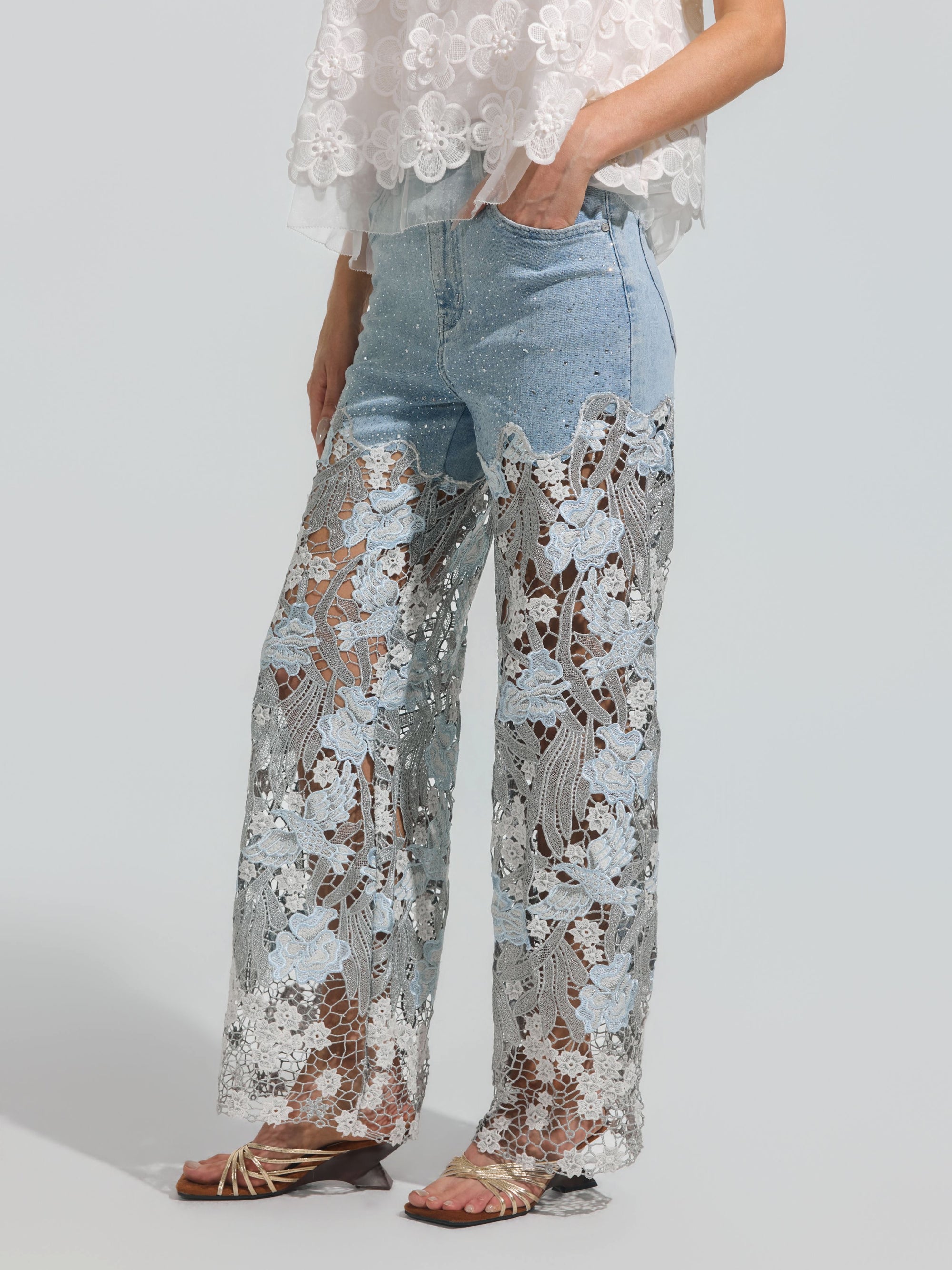 A person is seen from the waist down wearing Social Queen’s Floral Lace Patchwork Pants—light blue stretch denim jeans featuring sheer floral lace patchwork from mid-thigh to hem—styled with a white floral lace top and flat sandals.