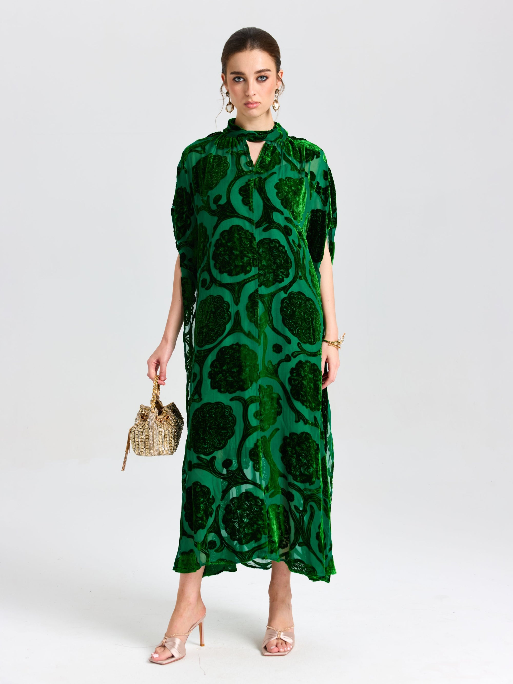 Woman wearing Social Queen’s Floral Velvet Cape Dress (Cami Included), featuring a bold pattern, styled with a small woven handbag, and standing against a plain white background.