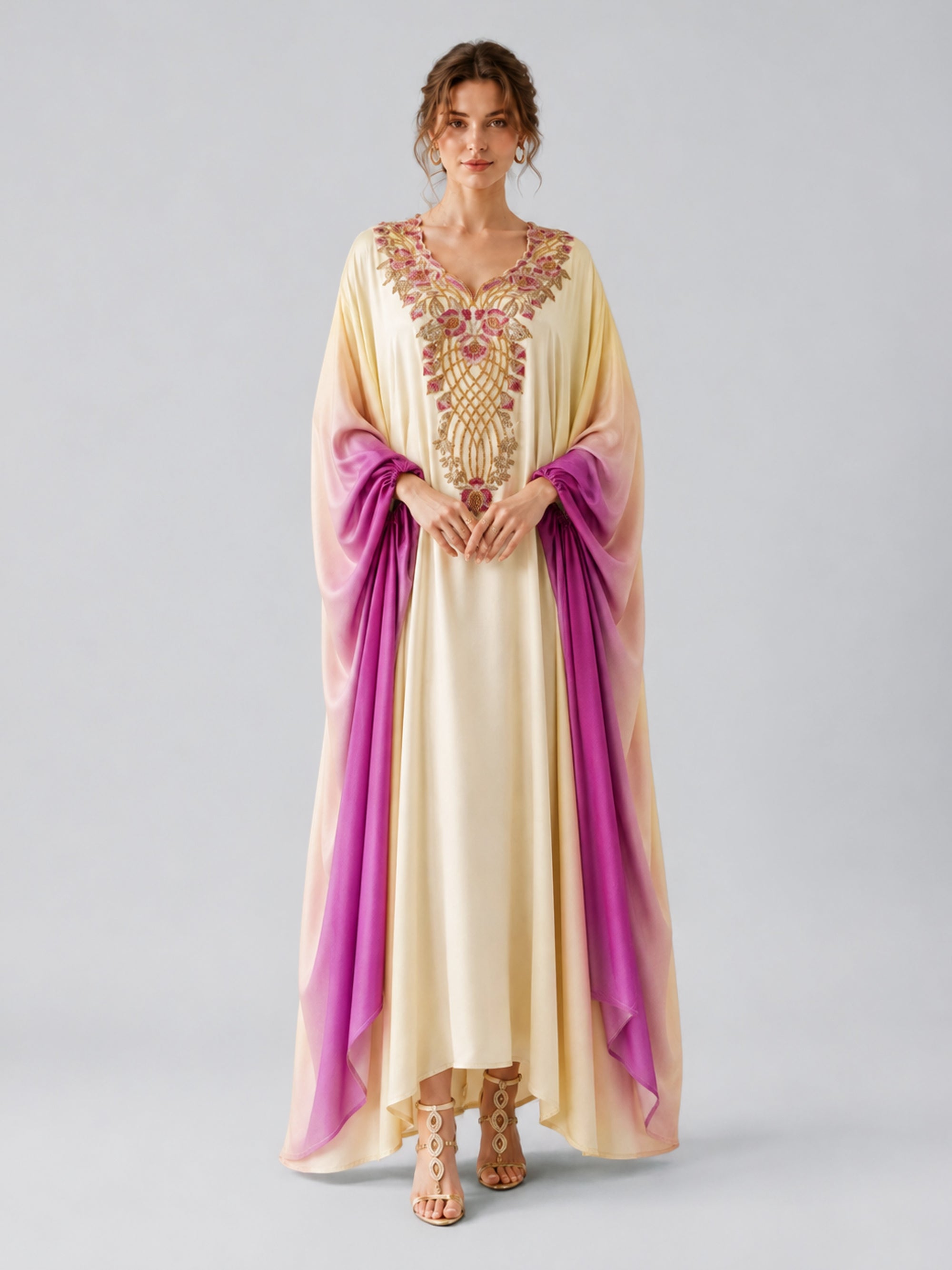 A woman stands against a plain light gray background, hands clasped in front, wearing the Ombré Beaded Embroidered Cape Dress by Social Queen—a cream and purple caftan adorned with intricate pink and gold floral beadwork.