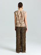 A woman stands facing away, wearing a beige floral short-sleeve top and Social Queen Sequin Fringe Wide-Leg Pants, set against a plain light background.