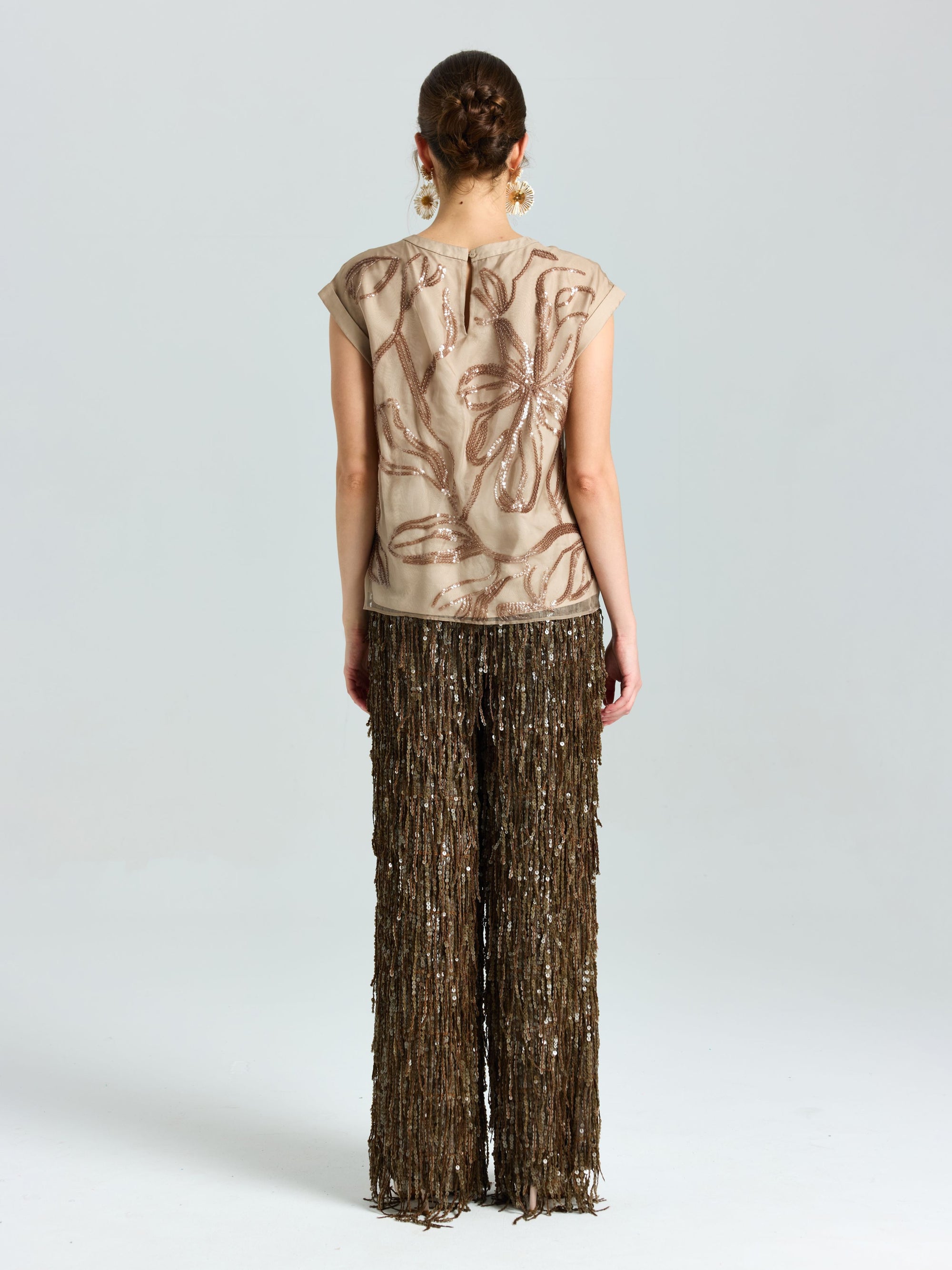 A woman stands facing away, wearing a beige floral short-sleeve top and Social Queen Sequin Fringe Wide-Leg Pants, set against a plain light background.