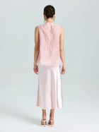 A woman stands facing away, wearing the Social Queen Floral Bird Embroidered Silk Top in light pink with lace details, paired with a satin midi skirt and nude high heels.