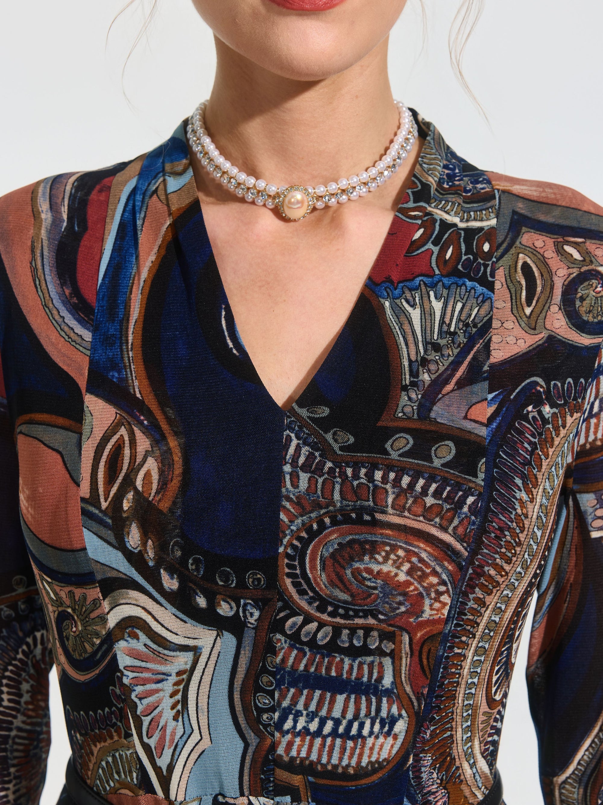 A woman wearing a Paisley Print Knit Dress by Social Queen (belt included) and a double-strand pearl choker necklace with a cameo pendant.