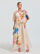 A woman stands against a plain background wearing the Social Queen Watercolor Floral Print Appliqué Dress, featuring sheer organza, an A-line silhouette, bold colorful florals, and puffed short sleeves.