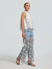 A woman stands in profile against a plain background, wearing the Social Queen 3D Floral Lace Appliqué Silk Top, paired with sheer lace wide-leg pants layered over light blue jeans and open-toed sandals.
