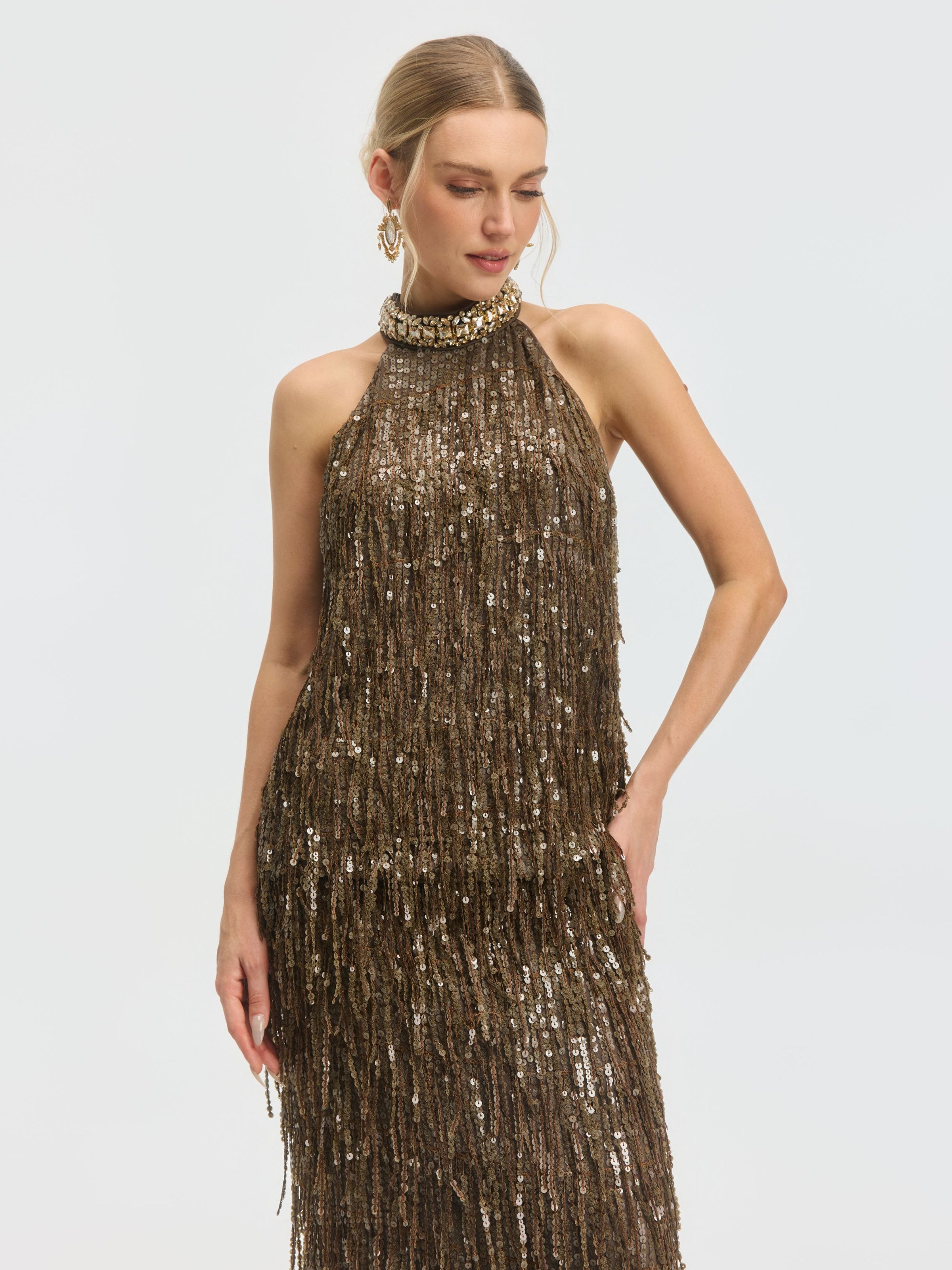 A woman models the Social Queen Beaded Sequin Fringe Halter Top, featuring a sleeveless design and shimmering brown sequins, posing with one hand on her hip against a plain background.