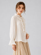 A person models the Social Queen Pearl Embellished Ruffle Collar Blouse, featuring long sleeves, paired with a beige floral skirt against a plain light gray background.