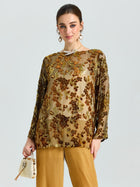 A woman wears the Social Queen Flocked Floral Silk Sheer Top (Camisole Not Included) with gold pants, carrying a small cream handbag against a plain background.