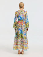 A woman faces away in the Social Queen Garden Print Silk Maxi Dress, featuring long sleeves and vibrant colors, styled with high heels and her hair in a neat bun.