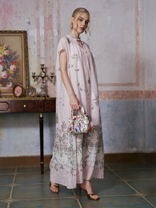 A woman stands indoors wearing the Social Queen Baroque Garden Print Ramie Dress (includes slip dress), holding a colorful handbag, with a floral painting and a candelabra on a wooden table in the background.