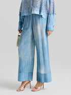A person models Social Queen's Washed Silk Wide-Leg Pants in light blue, styled with a lacy blue top, metallic open-toe heels, and a white handbag against a plain background.