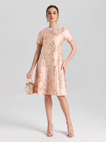 A woman in the Social Queen Pearl Embellished Jacquard Dress, accessorized with a pearl necklace, earrings, heels, and a small handbag, stands against a plain light background.
