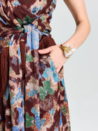 A person wears Social Queen's Floral Print Wide-Leg Pants, styled with one hand in a pocket and a gold and white floral bracelet—an ideal vacation look.