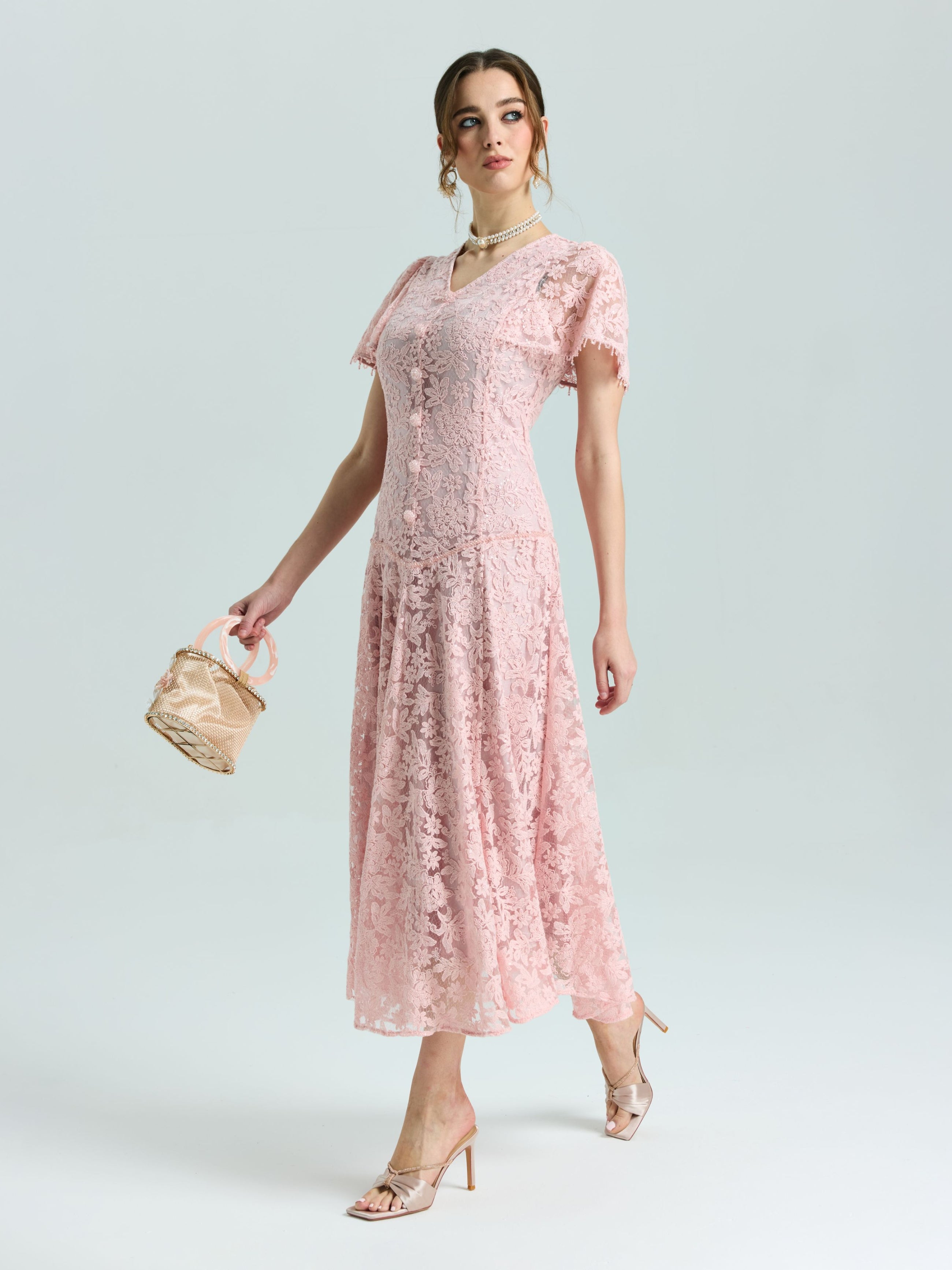 A woman wears the Social Queen Floral Embroidered Lace Dress in pink with an A-line silhouette, paired with a small beige handbag and heels, standing against a plain light background.