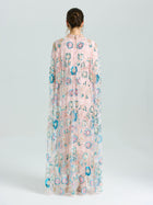 A person faces away in the Social Queen Beaded Floral Embellished Cape Gown, featuring sheer pink fabric with multicolored floral beading and sequins, set against a plain light background.