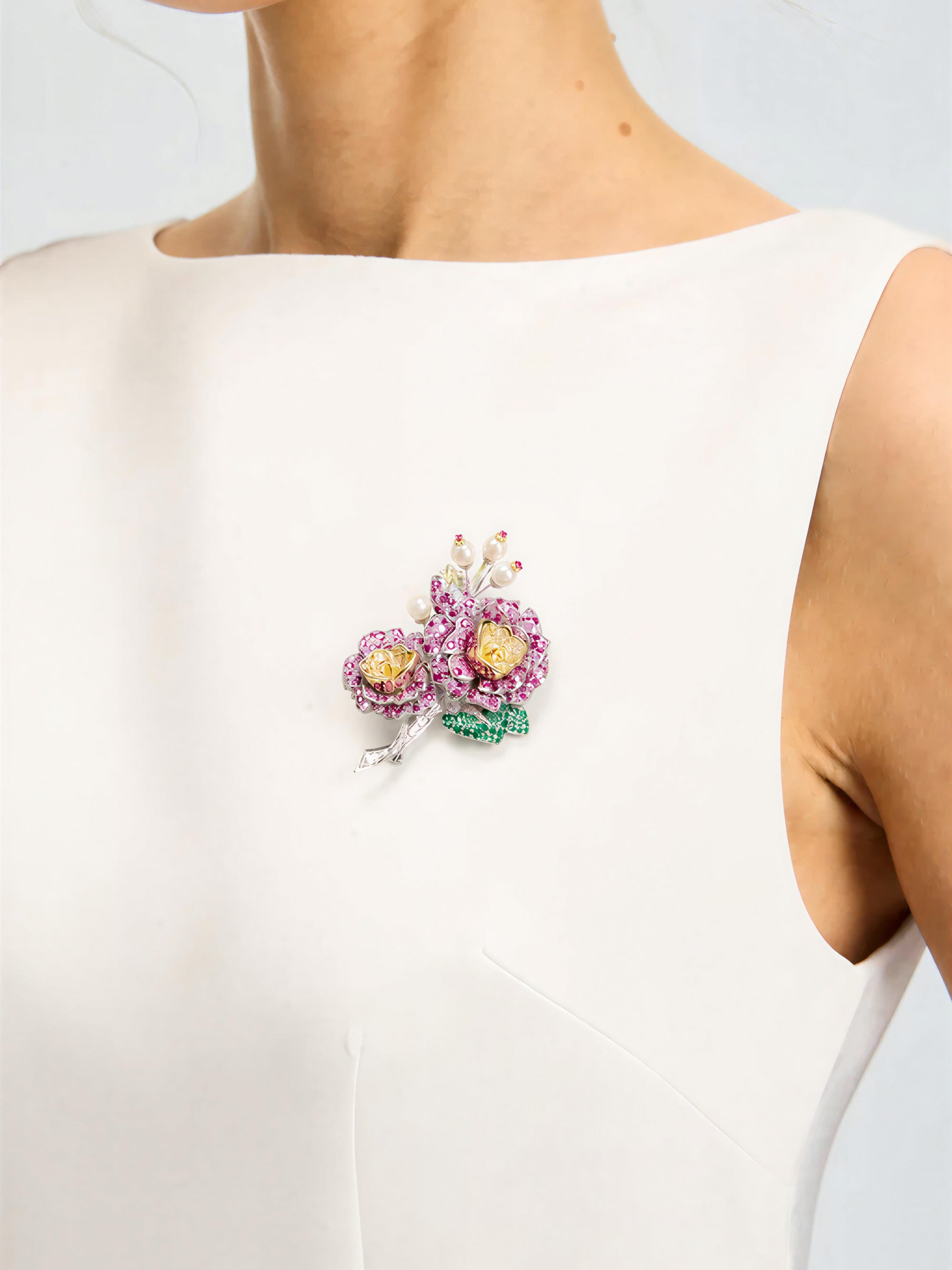 A woman in a sleeveless white dress wears the Social Queen “Camellia Bouquet Gemstone Brooch,” adorned with pink, yellow, and green stones, pinned to her left shoulder.