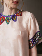 A woman wears the Paisley Garden Print Jacquard Silk Dress by Social Queen, featuring a light pink jacquard fabric with colorful embroidered patterns on the collar and sleeves. Only her lower face and upper torso are visible.