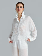 A woman models the Social Queen 3D Lace Appliqué Shirt—a sheer white long-sleeve blouse featuring elegant rose vine lace details—paired with matching white pants, set against a plain gray background.