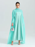 A woman in the Social Queen Beaded Cape Scarf Gown with an A-line silhouette stands against a white background, accessorized with a small silver handbag and matching silver heels.