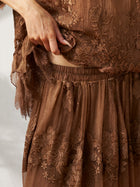 A person lifts the hem of the Social Queen 3D Floral Embroidered 100% Silk Ruffle Skirt, revealing part of their waist and the skirt’s waistband.