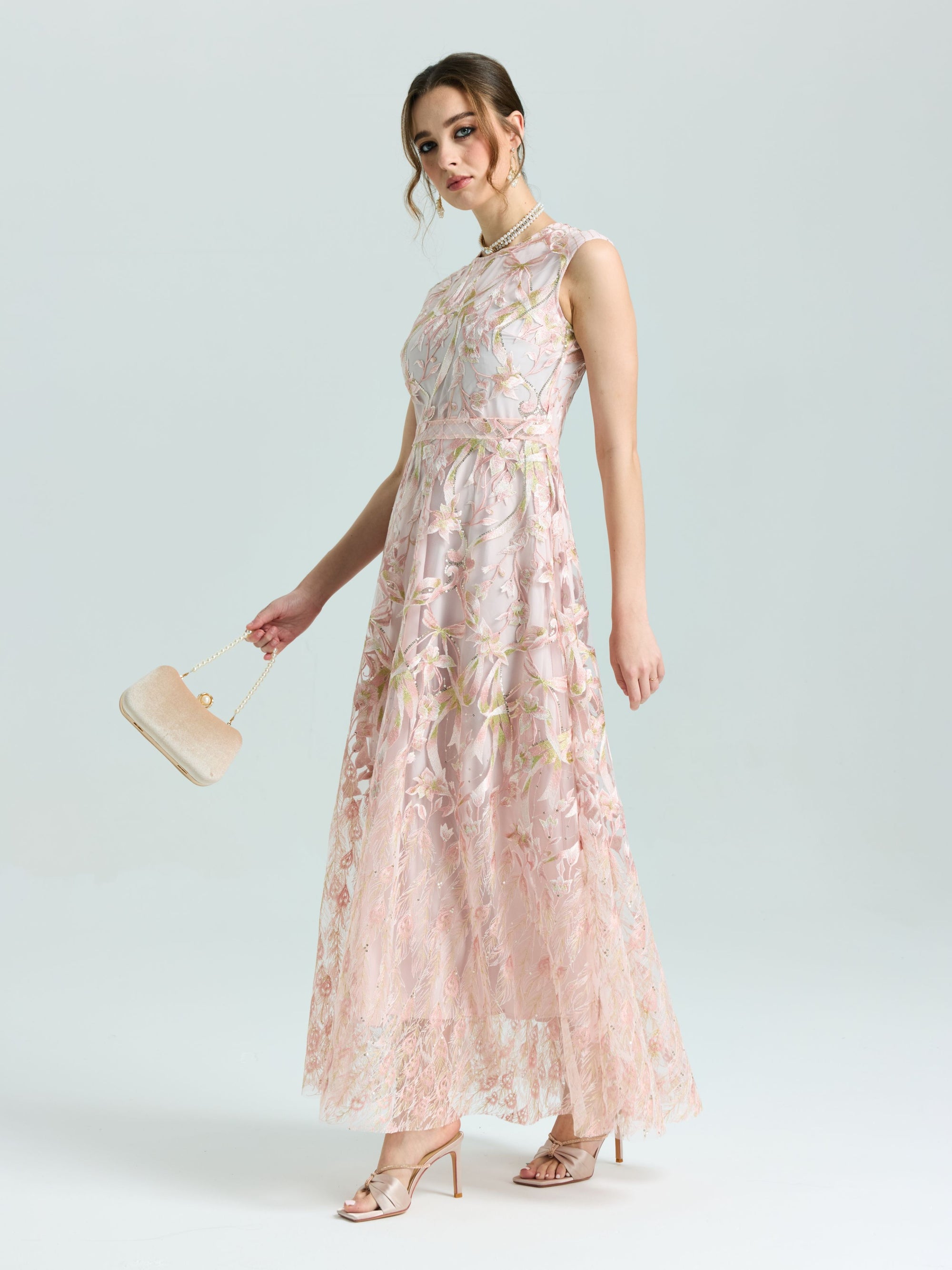 A woman wears the Social Queen Gold Floral Embroidered Dress, a sleeveless, floor-length A-line gown with gold floral details, paired with a beige clutch and matching open-toe heels against a plain background.
