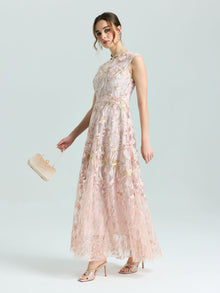 A woman wears the Social Queen Gold Floral Embroidered Dress, a sleeveless, floor-length A-line gown with gold floral details, paired with a beige clutch and matching open-toe heels against a plain background.