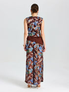 A woman faces away, wearing Social Queen Floral Print Wide-Leg Pants in brown, blue, and beige with a matching sleeveless top and fringe at the waist.