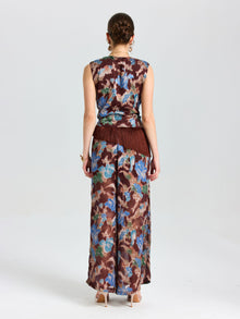 A woman faces away, wearing Social Queen Floral Print Wide-Leg Pants in brown, blue, and beige with a matching sleeveless top and fringe at the waist.