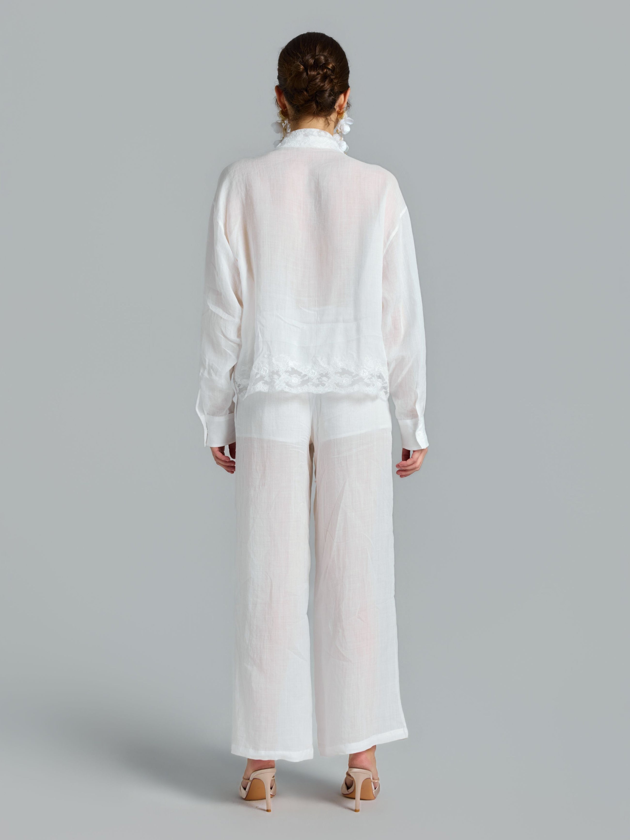 A person stands with their back to the camera, modeling Social Queen’s Textured Straight-Leg Pants—a lightweight, slub-textured style with a relaxed fit—paired with a sheer white long-sleeve top and beige heeled sandals, set against a plain gray background.