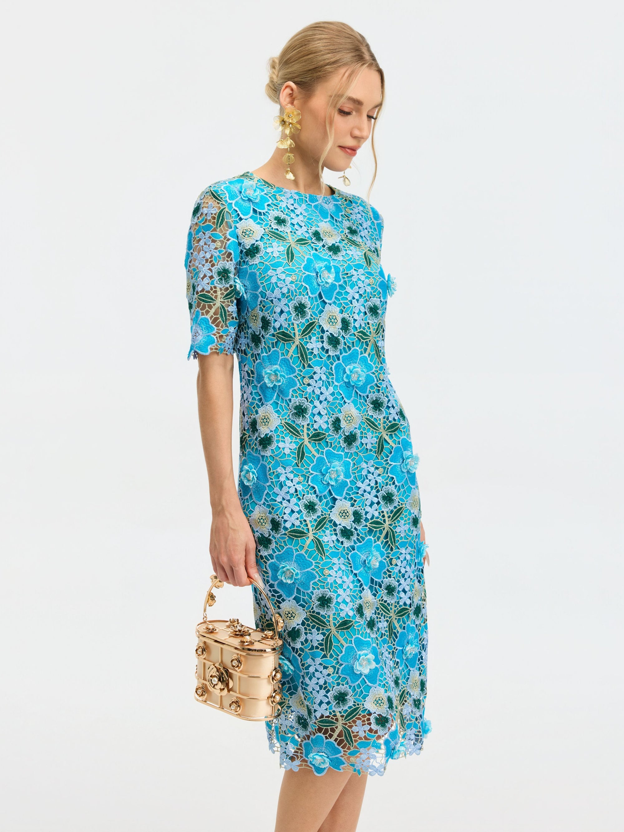 A woman in the Social Queen Floral Appliqué Lace Shift Dress holds a small gold handbag and looks downward against a plain white background.