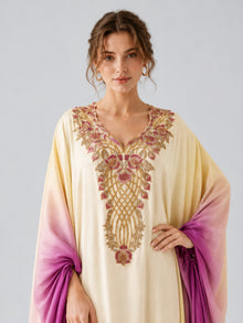 A woman wearing the Social Queen Ombré Beaded Embroidered Cape Dress in cream and purple satin, featuring a gold and pink embroidered neckline, stands against a plain light background.