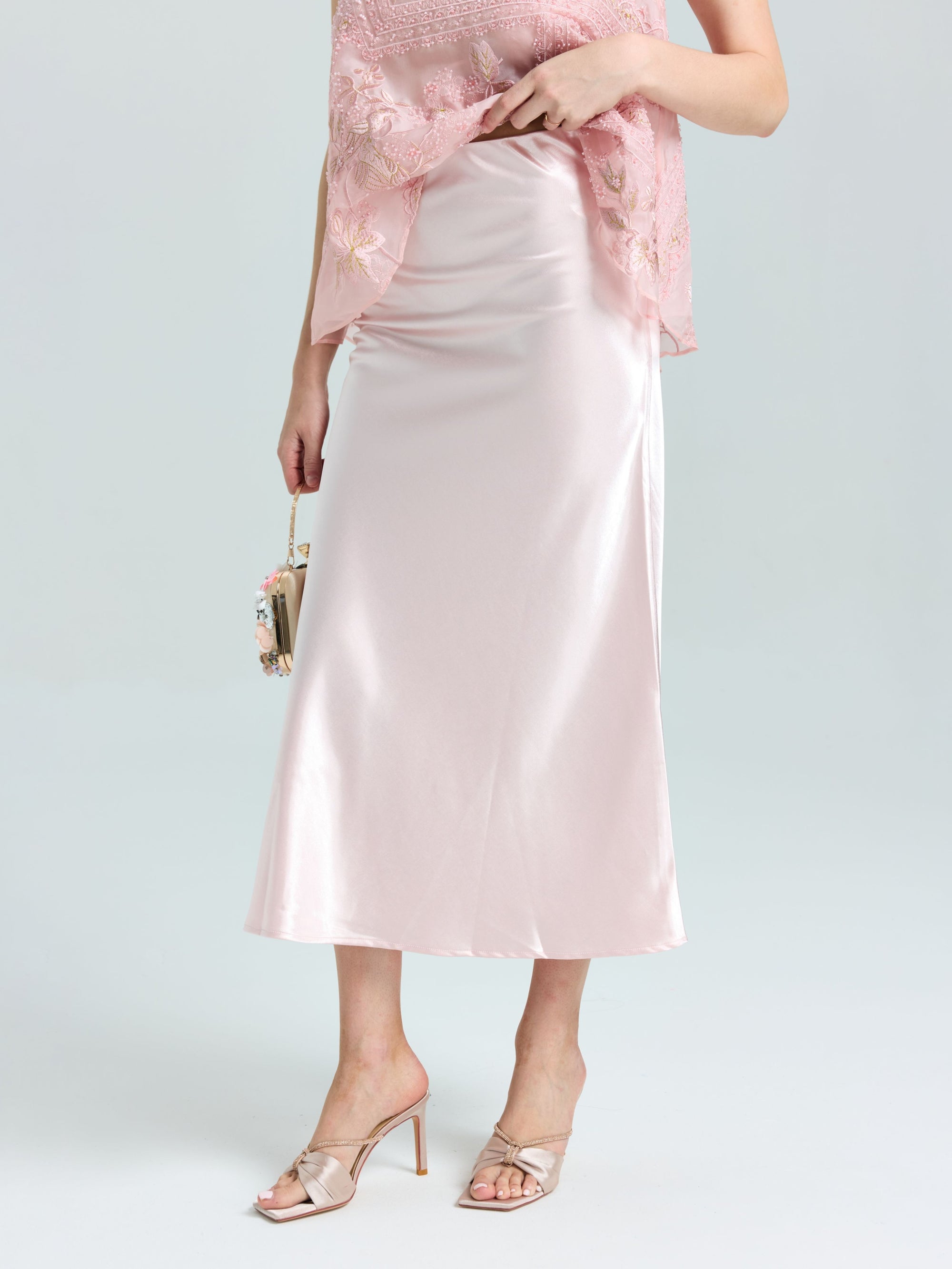 A person in the Social Queen Satin A-Line Midi Skirt, paired with a lace top, heeled sandals, and a small handbag, stands against a plain background.