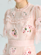A woman wears the Social Queen Embroidered Ruffle Tiered Tulle Dress, featuring light pink tulle, ruffles, sequin floral appliqués, sheer sleeves, and a pleated waistband—ideal for special occasions.