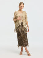 A woman stands against a white background, elegantly draping the Social Queen Pearl Floral Appliqué Fringe Cape over her shoulders, styled with a textured beige top, metallic fringed skirt, gold sandals, and statement earrings.