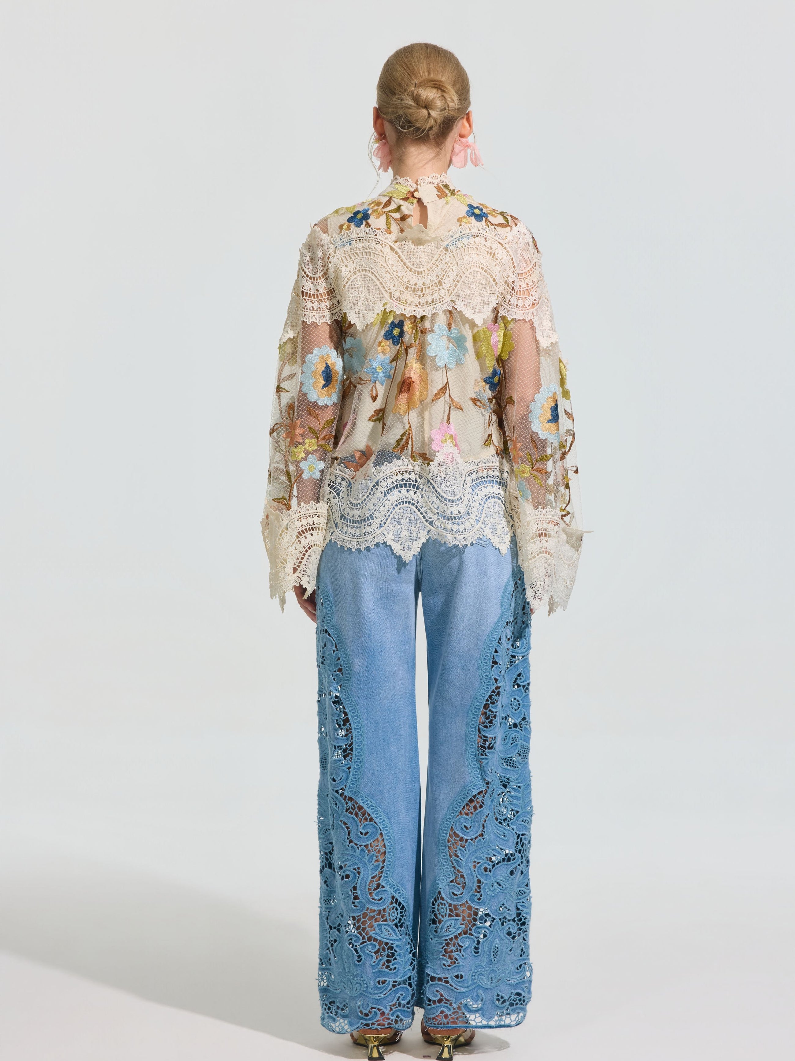 A woman faces away, wearing the Social Queen Floral Embroidered Lace Trim Top paired with light blue wide-leg denim pants featuring intricate lace detailing.